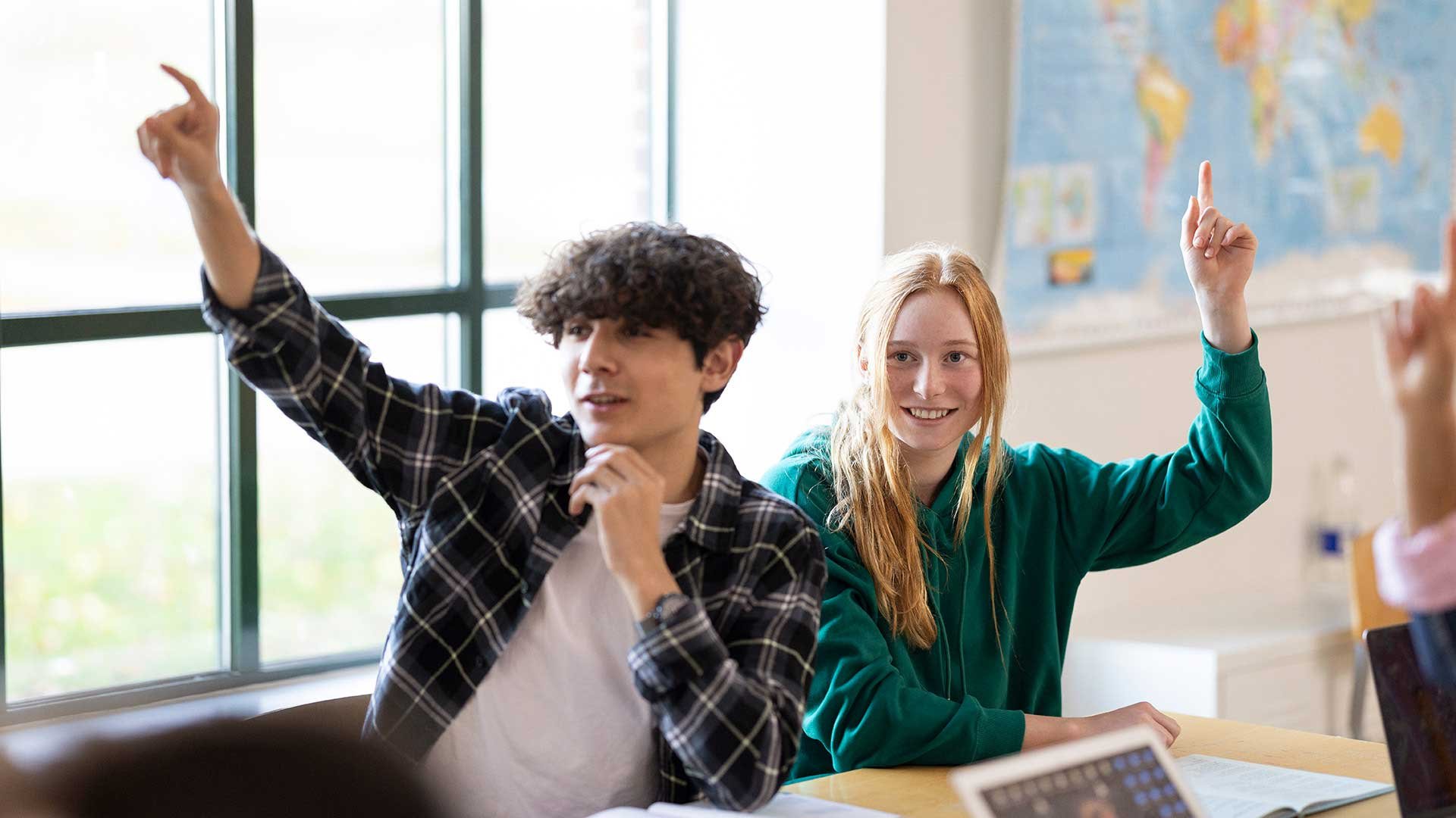 Pojke och flicka i klassrum, räcker upp handen.