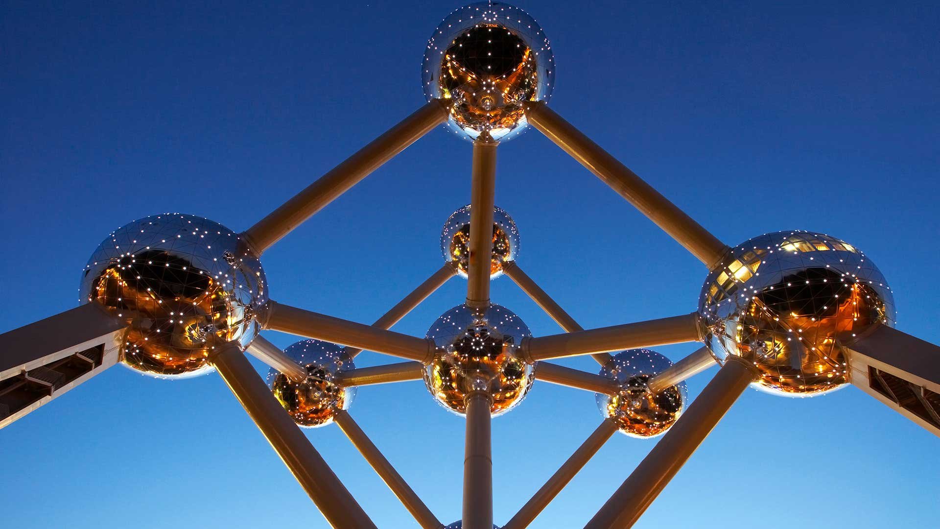 Auf dem Bild ist so etwas wie Skulptur abgebildet. Sie besteht aus mehreren Metallkugeln die miteinander mit Metallstangen verbunden sind. Im Hintergrund ist nur ein blauer Himmel.