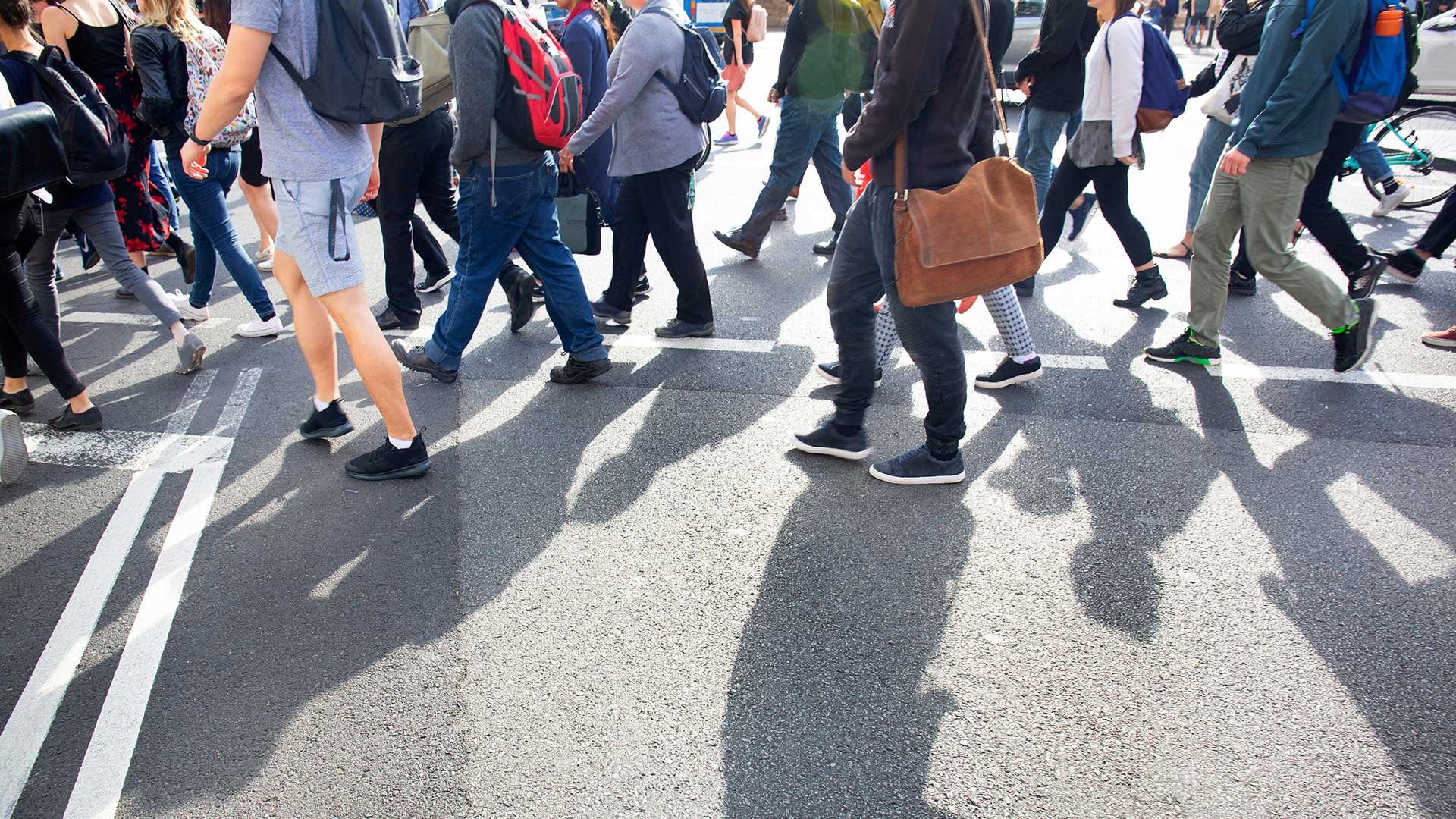 Många människor går över gata. Bilden är beskuren så att inga huvuden syns.