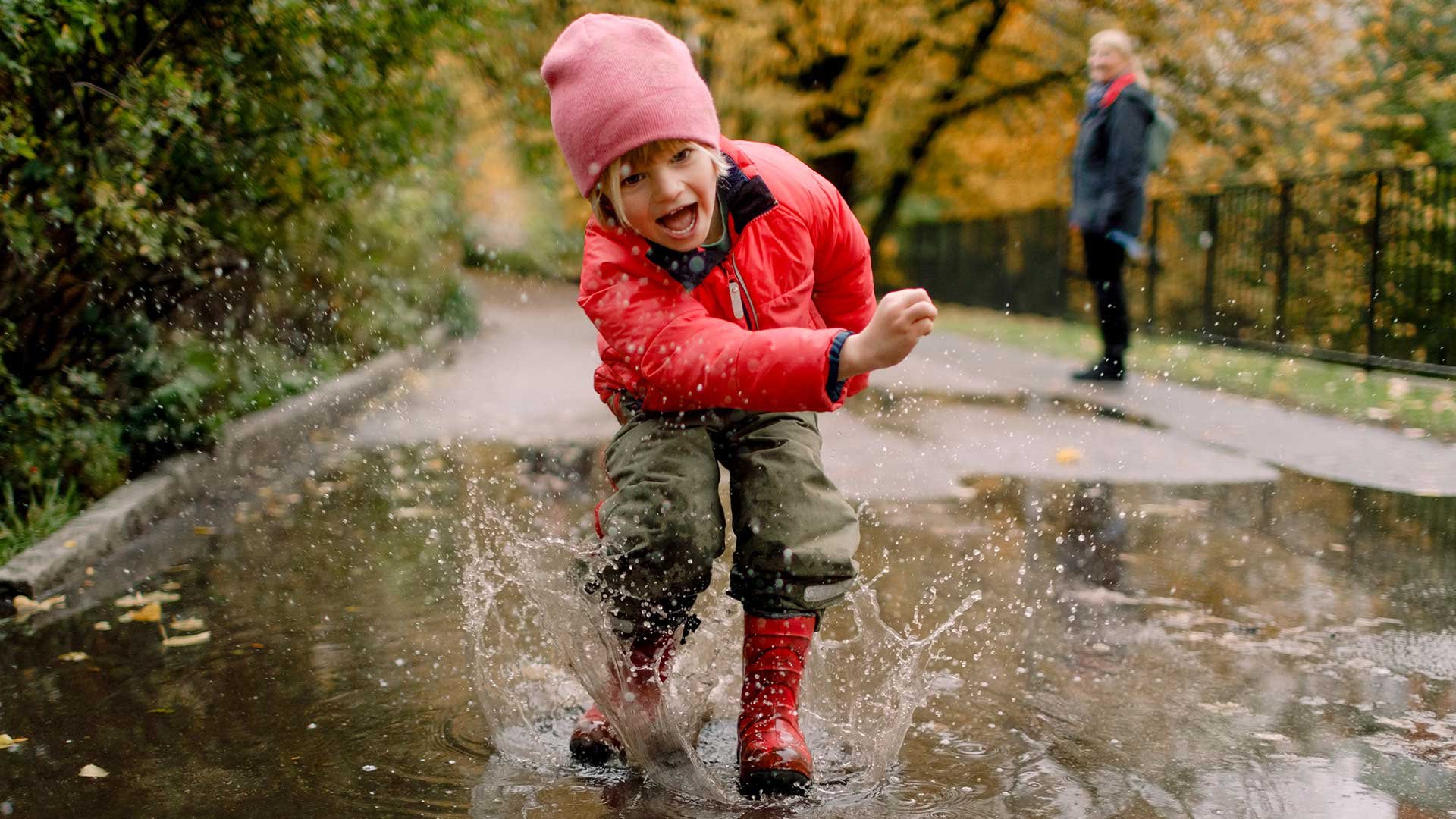 Barn plaskar i vattenpöl vid höstskrudad skog